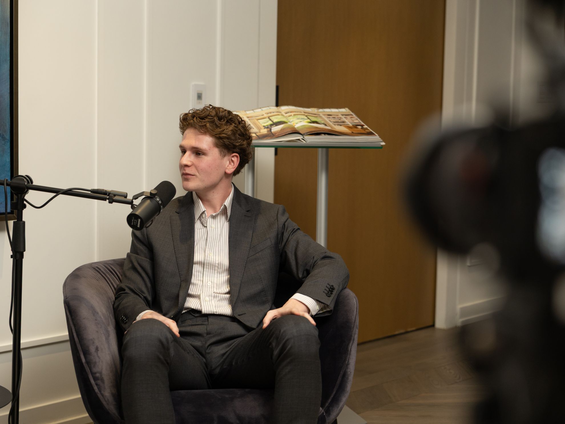 A guest leaning in to speak beside a microphone, with a camera out of focus in the foreground