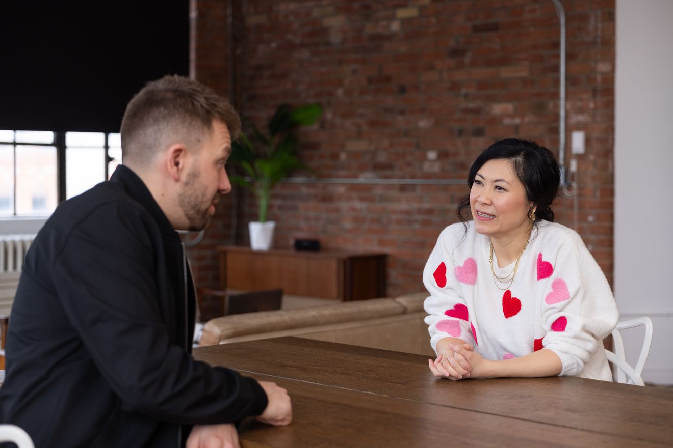 Host and guest talking across a wooden table in the brick loft
