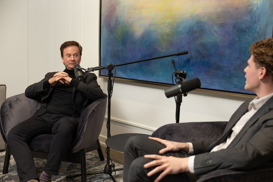 Two men talking in armchairs in a bright room with a large painting