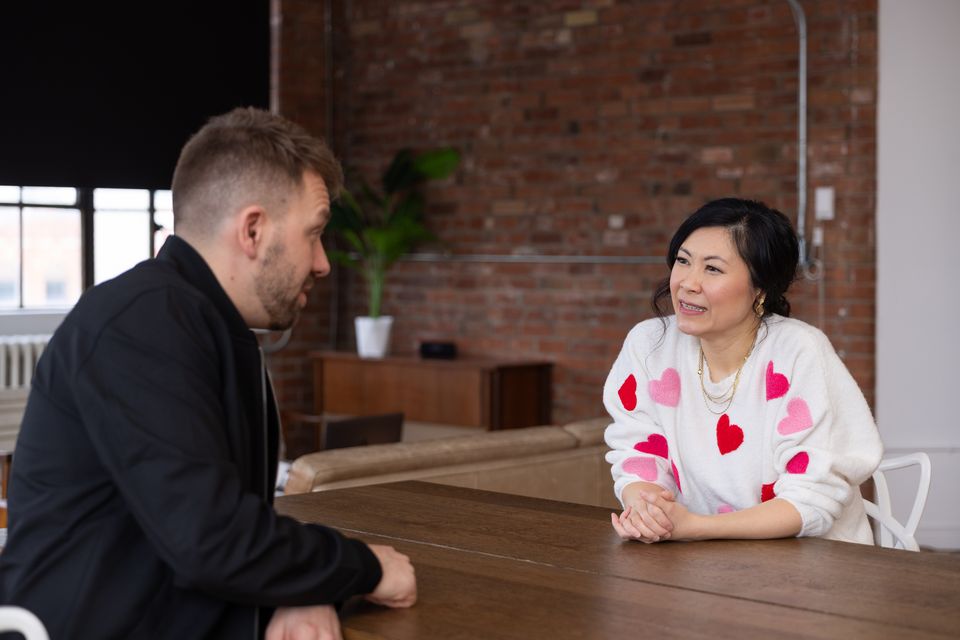 Two people in conversation across a wooden table in a brick loft