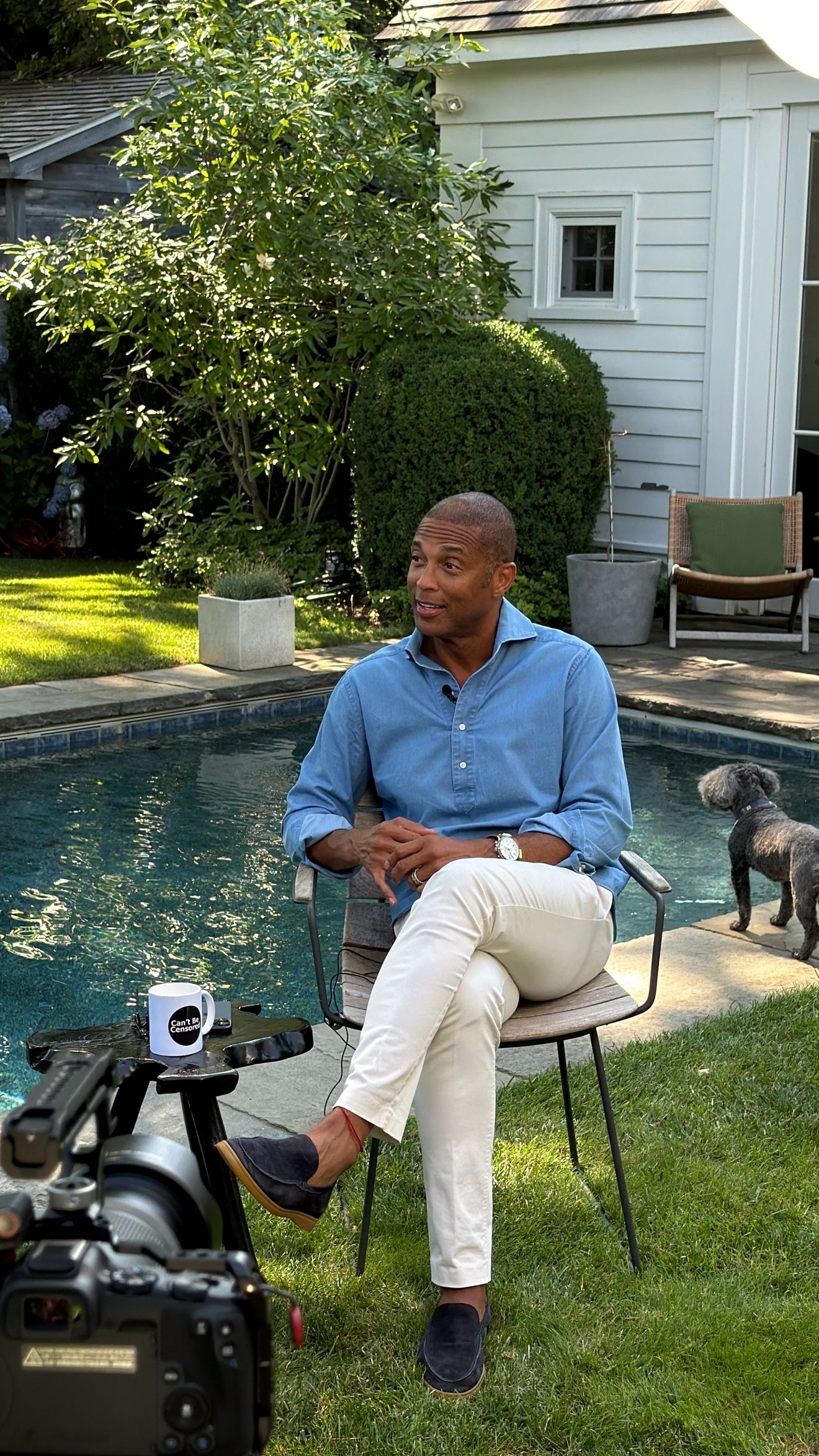 A guest seated in a garden beside a swimming pool, with a camera in the foreground